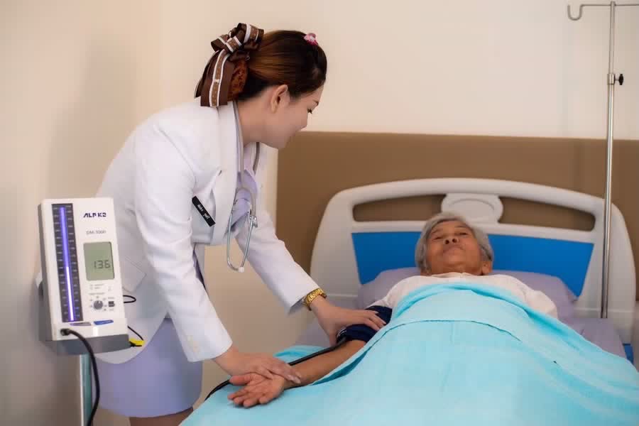 พยาบาลวัดความดันโลหิตให้ผู้สูงอายุที่พักบนเตียง