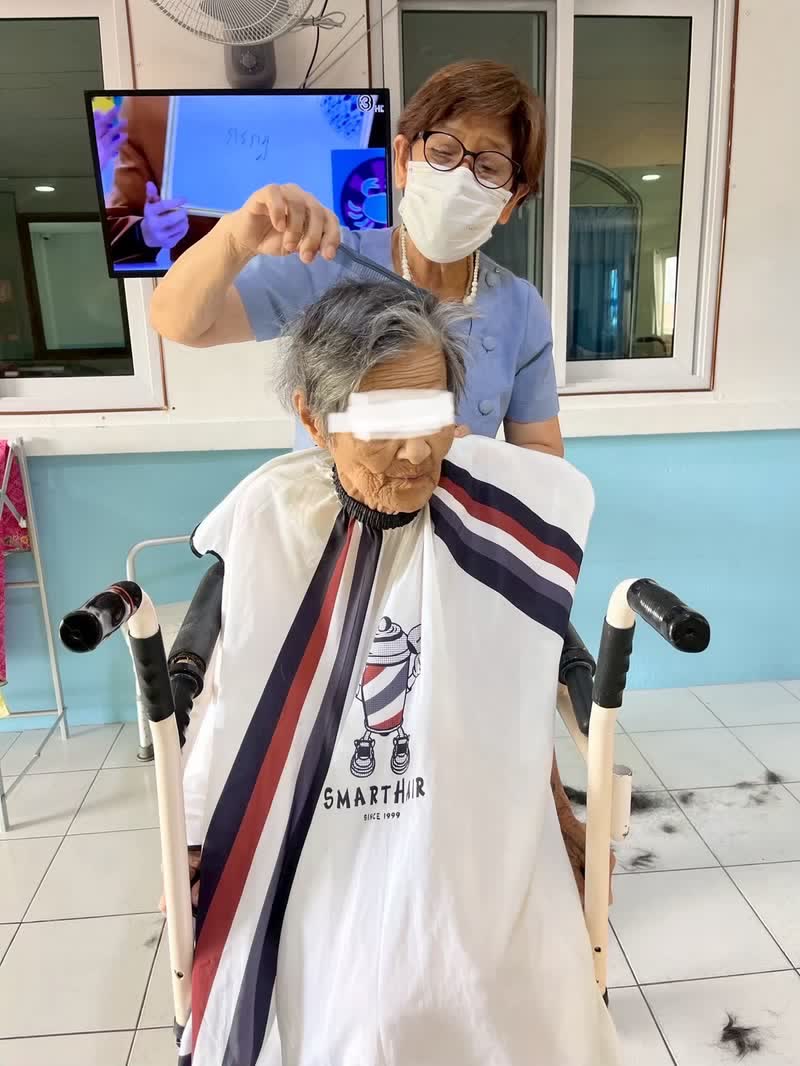 เจ้าหน้าที่ตัดผมให้ผู้สูงอายุที่นั่งบนเก้าอี้เคลื่อนย้ายในพื้นที่ส่วนกลาง
