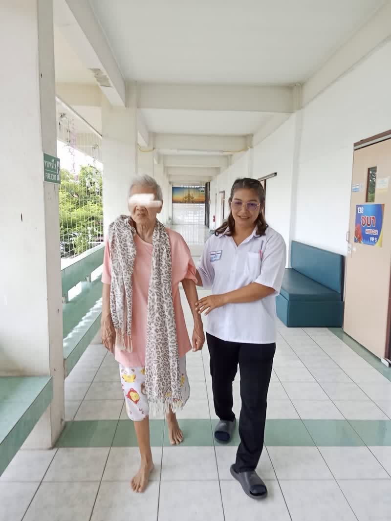 เจ้าหน้าที่ประคองผู้สูงอายุเดินไปตามทางเดินภายในอาคาร